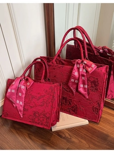 Elegant red jacquard wedding tote bag set with festive ribbons on a wooden floor