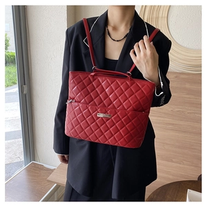 Close-up of red quilted shoulder tote bag with silver metal logo and zip pocket detail