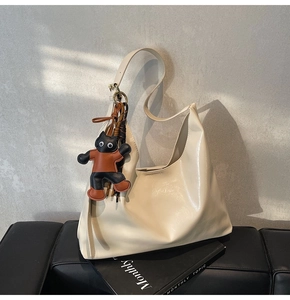 Close-up of a cream hobo tote bag on a black bench with a cute cat charm accessory