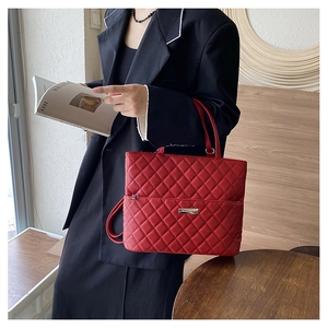 Detail of red quilted tote bag featuring metal plaque and practical front zipper pocket