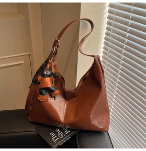 Macro shot of brown patent leather tote with a playful cartoon cat pendant on black sofa