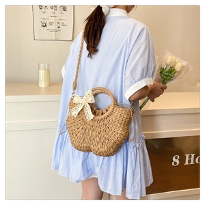Detail of straw crossbody bag with white lace bow and drawstring closure on beach bag