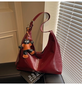 Detail of burgundy textured patent leather Hobo bag with a cartoon cat charm on a sofa
