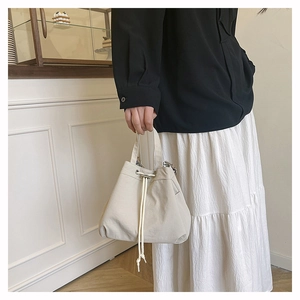 Detail of a minimalist cream nylon drawstring bucket bag held by a model in casual style
