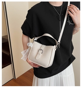 Detail of cream bucket bag featuring silver buckle and elegant white lace ribbon ornament