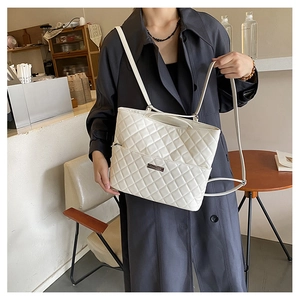 Close-up of white quilted tote bag with silver brand plaque and textured PU leather