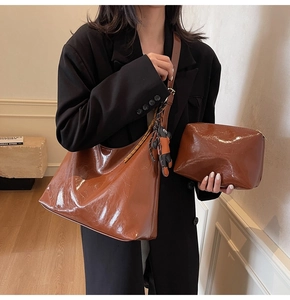 Detail of a shiny brown leather tote bag with a cartoon bear charm and a small matching pouch