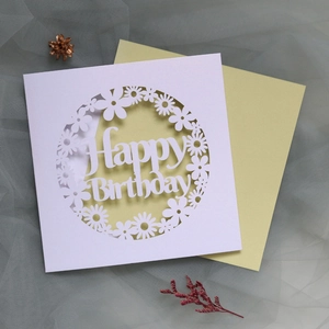 Detail of laser-cut white Happy Birthday card with floral wreath design and yellow envelope