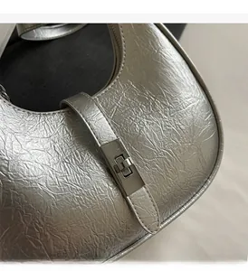 Detail of silver metallic handbag featuring textured pleats and a metal turn-lock closure