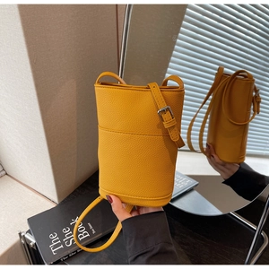 Detail view of ginger yellow lychee grain bucket bag reflected in a mirror surface