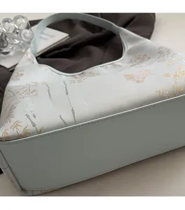 Detail of light blue handbag featuring elegant butterfly and bamboo leaf embroidery