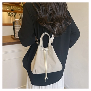 Minimalist beige nylon bucket bag with drawstring closure and adjustable strap on a woman