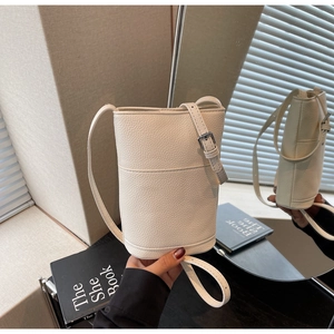 Macro detail of white lychee pattern leather and silver hardware on a crossbody bucket bag