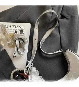 Detail of silver dumpling bag with metallic texture, pearl charm, and long shoulder strap
