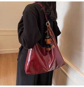 Macro detail of glossy burgundy tote bag with gold ring buckle and cute cat plush charm