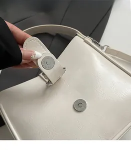 Detail of the magnetic buckle closure on a cream leather bucket bag with silver hardware