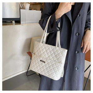 Close-up of white quilted tote bag featuring metal logo plate and elegant diamond texture