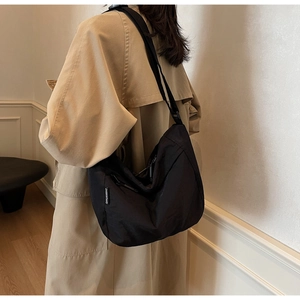 Side view of large black nylon crossbody bag worn with khaki trench coat