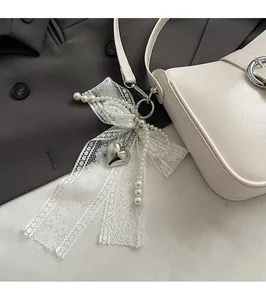 Close-up of elegant lace bow with pearls and silver heart pendant on a leather handbag