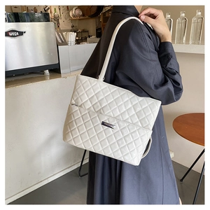 Close-up of white quilted tote bag with silver metal plaque and fine shoulder straps