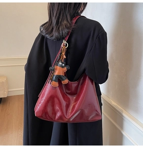 Detail of burgundy glossy leather tote bag with a cute cat charm on the shoulder strap