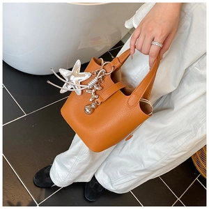 Detalle de bolso cubo naranja en cuero granulado con colgantes de estrella y perro