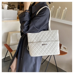 Close-up of white quilted tote bag with silver metal logo and leather shoulder straps