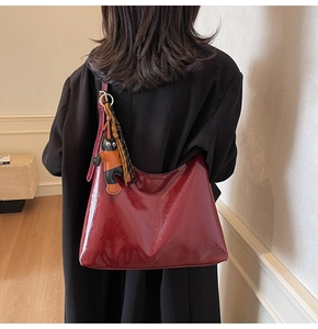 Detail of burgundy patent leather hobo bag with cat charm and tassel decoration
