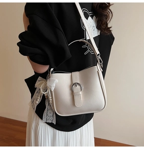 Detail of cream white shoulder bag featuring lace bow and pearl charm with metal buckle