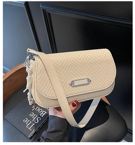 Détail d'un sac bandoulière tissé beige avec logo en métal et pompon en cordelette