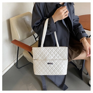 Detail of white quilted leather tote bag featuring silver brand tag and diamond stitching
