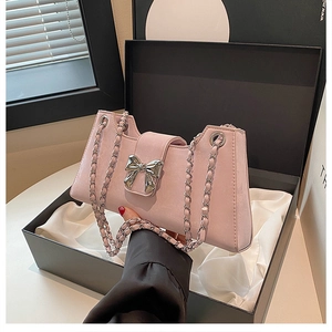Détail d'un sac à bandoulière rose avec nœud argenté dans une boîte cadeau de luxe
