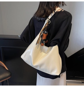 View of a large white glossy hobo bag on shoulder with a cute cartoon charm accessory