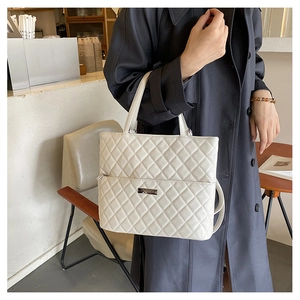 Detail of quilted beige tote bag with silver logo plaque and stylish decorative zipper