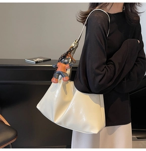 Side view of a cream leather tote bag with a cartoon charm on a commuter model