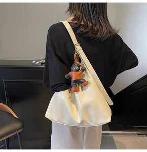Detail of cream patent leather tote bag with a whimsical monster charm on a shoulder strap