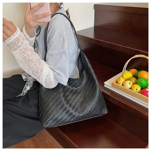Detail of black woven leather hobo bag with intricate cross weave texture on wooden stairs
