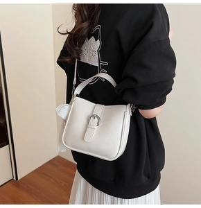 Detail of off-white shoulder bucket bag with silver buckle and lace bow on a model