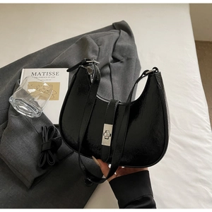 Detail of black glossy hobo bag with silver clasp on a grey suit jacket backdrop
