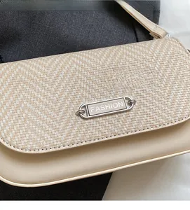 Détail du sac à bandoulière en tissu beige tressé avec plaque métallique et similicuir