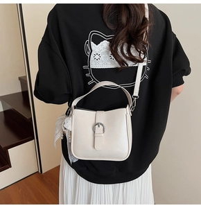 Detail view of cream shoulder bag with silver ring buckle and pearl lace charm on model