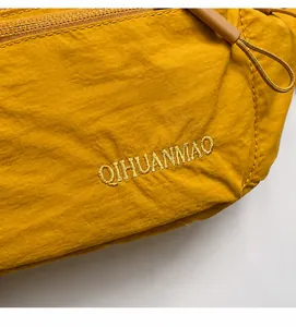 Detail of ginger yellow crossbody bag showing nylon texture and brand embroidery