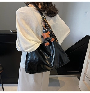 Detail of glossy black patent leather tote bag with unique cat charm and woven cord