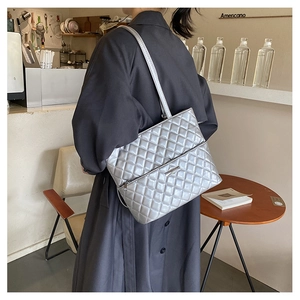 Silver quilted tote bag with metallic finish shown on model in a cafe setting