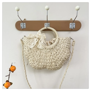 Detail of a woven straw semi-circle bag featuring a delicate lace bow and drawstring liner