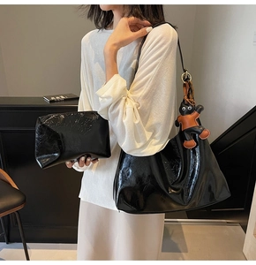 Detail of glossy black tote bag and clutch set with cat charm on white outfit