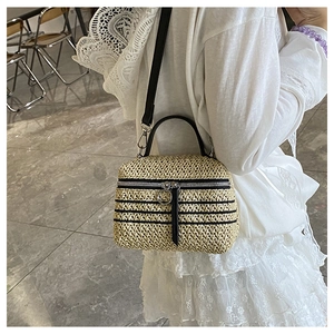 Détail du sac boîte en paille tressée avec poignée en cuir noir et grand anneau de fermeture