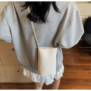 Close-up of minimalist cream-white grain leather crossbody phone bag on shoulder