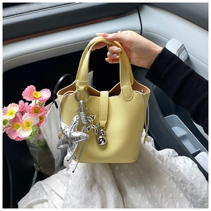 Detalle de bolso bucket amarillo en cuero granulado con adornos plateados y asa