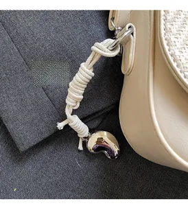 Détail macro d'un sac en tweed beige avec cordon en coton et pendentif fève en argent